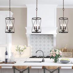 three lights hanging from the ceiling over a kitchen island with flowers in vases on it