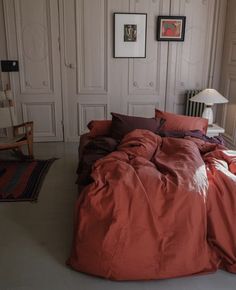 a bed with red sheets and pillows in a room next to white closets on the wall