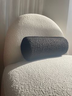 a white chair with a black pillow on it's back and curtain in the background