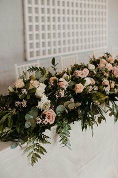 an arrangement of flowers and greenery on a white table cloth at a wedding reception