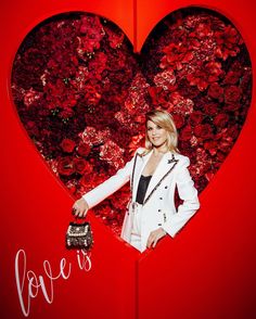 a woman standing in front of a red heart with roses on the wall behind her