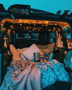 the back end of a van filled with blankets and pillows, lights strung from the ceiling