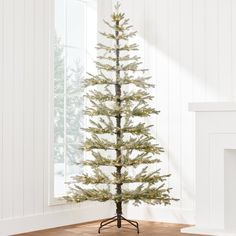 a small white christmas tree in front of a window with snow on the ground and wooden floor