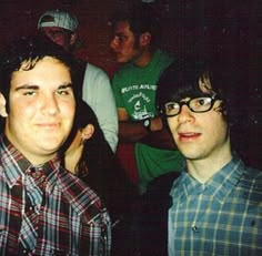 two young men standing next to each other in front of a group of people at a party