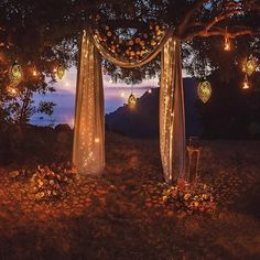 an outdoor wedding setup with lights strung from the trees and hanging lanterns on the ground