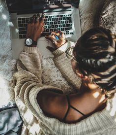 a woman sitting in front of a laptop computer on top of a white blanket covered floor