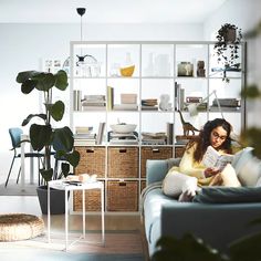 a woman sitting on a couch reading a book in a room with plants and bookshelves