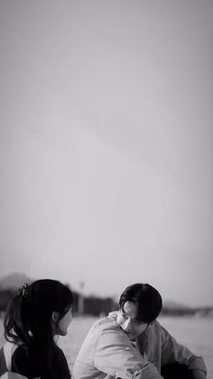 a man and woman sitting on top of a sandy beach