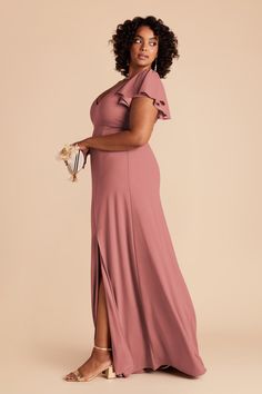 a woman in a pink dress poses with her hand on her hip, wearing heels