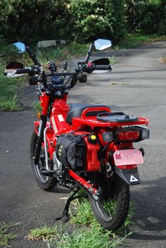 a red motorcycle parked on the side of a road next to some bushes and trees