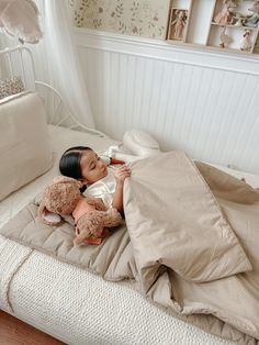 a small doll laying on top of a bed next to a teddy bear and pillow