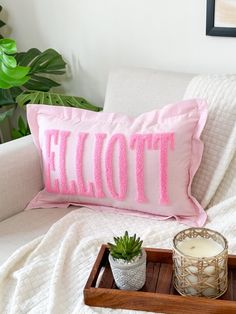 a pink pillow with the word toile on it next to a candle and potted plant