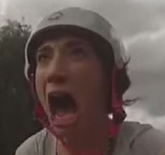 a man with his mouth open wearing a helmet and making a silly face while standing in front of some trees