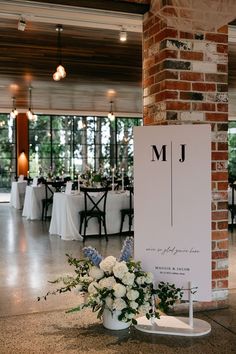 a sign that is sitting on the ground in front of some tables with flowers and chairs