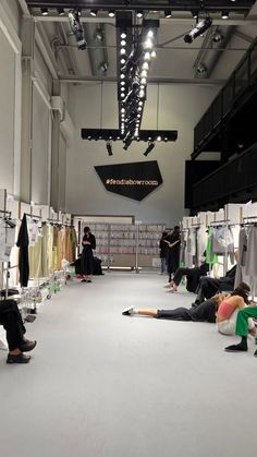 people are sitting on the floor in an open room with clothes hanging from the ceiling