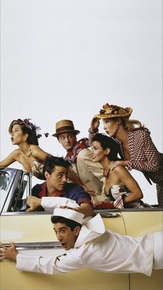 a group of people sitting on the roof of a car in front of a white wall