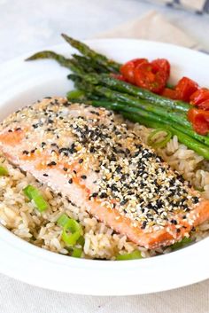 a white plate topped with salmon and rice covered in seasoning next to asparagus