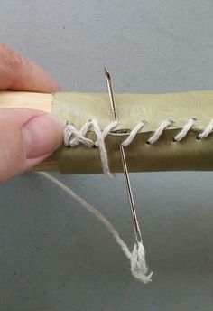 a person holding a pair of scissors next to a piece of leather with white thread on it