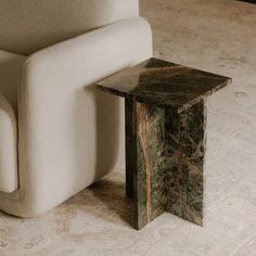 a marble side table sitting next to a white chair on a carpeted room floor