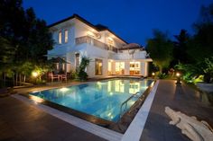 an outdoor swimming pool in front of a large white house at night with lights on