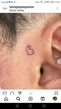 a close up of a person with a small bunny tattoo on their left side of the ear