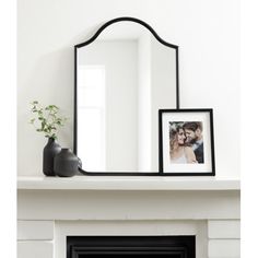 a fireplace with a mirror, vase and photo on the mantel top in front of it