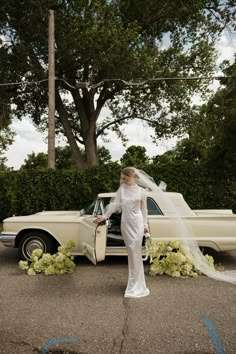 a woman standing in front of a car with a veil over her head and flowers on the ground