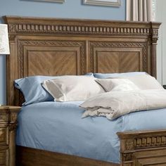 a bed with blue sheets and white pillows in a bedroom next to a lamp on a dresser