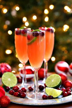 two glasses of wine with cranberries and limes on a plate in front of a christmas tree