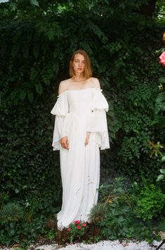 a woman standing in front of a bush wearing a white dress