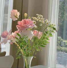 a vase filled with pink flowers sitting on top of a table next to a window