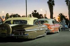 several classic cars are parked on the side of the road at night with palm trees in the background