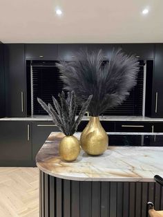 two gold vases with black feathers sit on a marble countertop in a kitchen