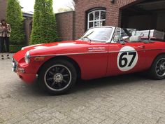 an old red sports car parked in front of a brick building with a number on it