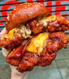 a hand holding a chicken sandwich with cheese and sauce