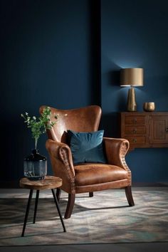 a brown chair sitting in front of a blue wall next to a table with a potted plant on it