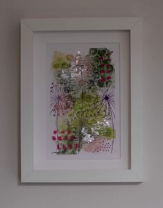 a white frame holds an art work with flowers and leaves in it on the wall