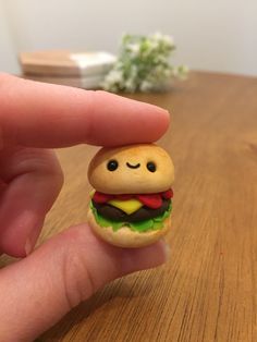 a hand holding a tiny toy hamburger on top of a wooden table