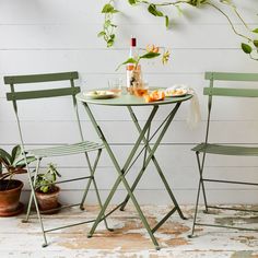 two green chairs and a table with food on it in front of a white wall