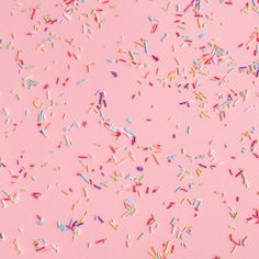 colorful sprinkles are scattered on a pink background