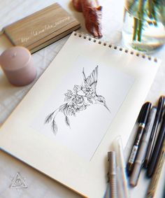 a drawing of a hummingbird with flowers on it's back is next to some pens and pencils