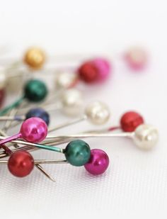 a bunch of pins with different colors and sizes on top of each other, sitting on a white surface