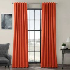 an orange curtain hanging in front of a window with a chair and table next to it