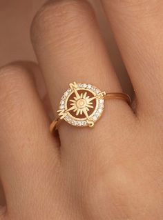 a woman's hand wearing a gold ring with a diamond compass on the middle