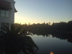 the sun is setting over a body of water near a house and palm tree in front of it