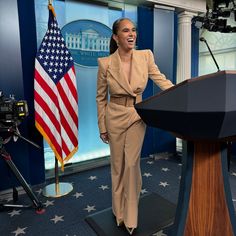 a woman standing at a podium in front of an american flag and the white house