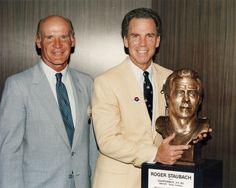 two men standing next to each other in front of a busturine holding a trophy