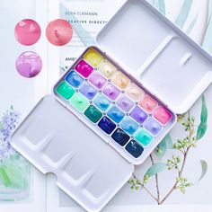 an open box of watercolors on top of a table with flowers and leaves