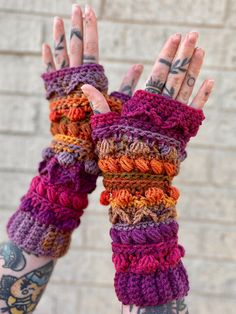 a person with tattoos holding their hands up to the camera wearing colorful knitted arm warmers