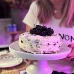 a woman is holding a cake on a white plate with blackberries and lavenders